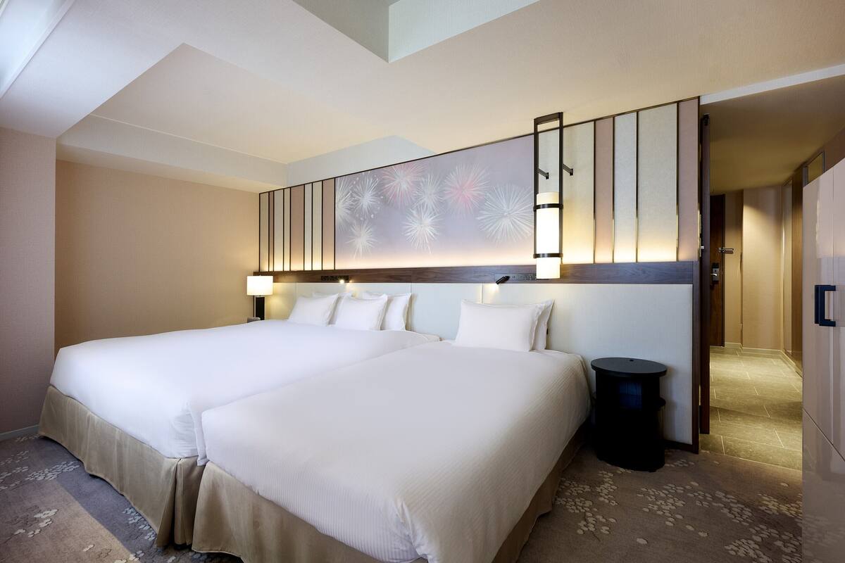 A hotel room with a large bed, a nightstand, a lamp, and a wall-mounted light fixture.