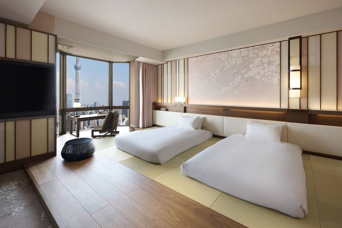 A hotel room with two beds, a TV, and a view of a cityscape.