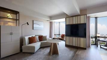 Una sala de estar moderna con un sofá, una mesita redonda, un televisor y vistas a la ciudad a través de amplias ventanas.