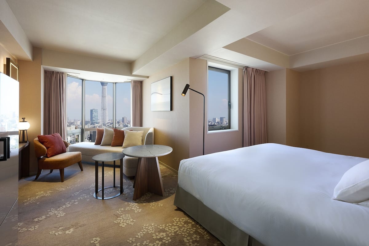 A hotel room with a bed, a sofa, a small table, a chair, and a desk with a lamp.