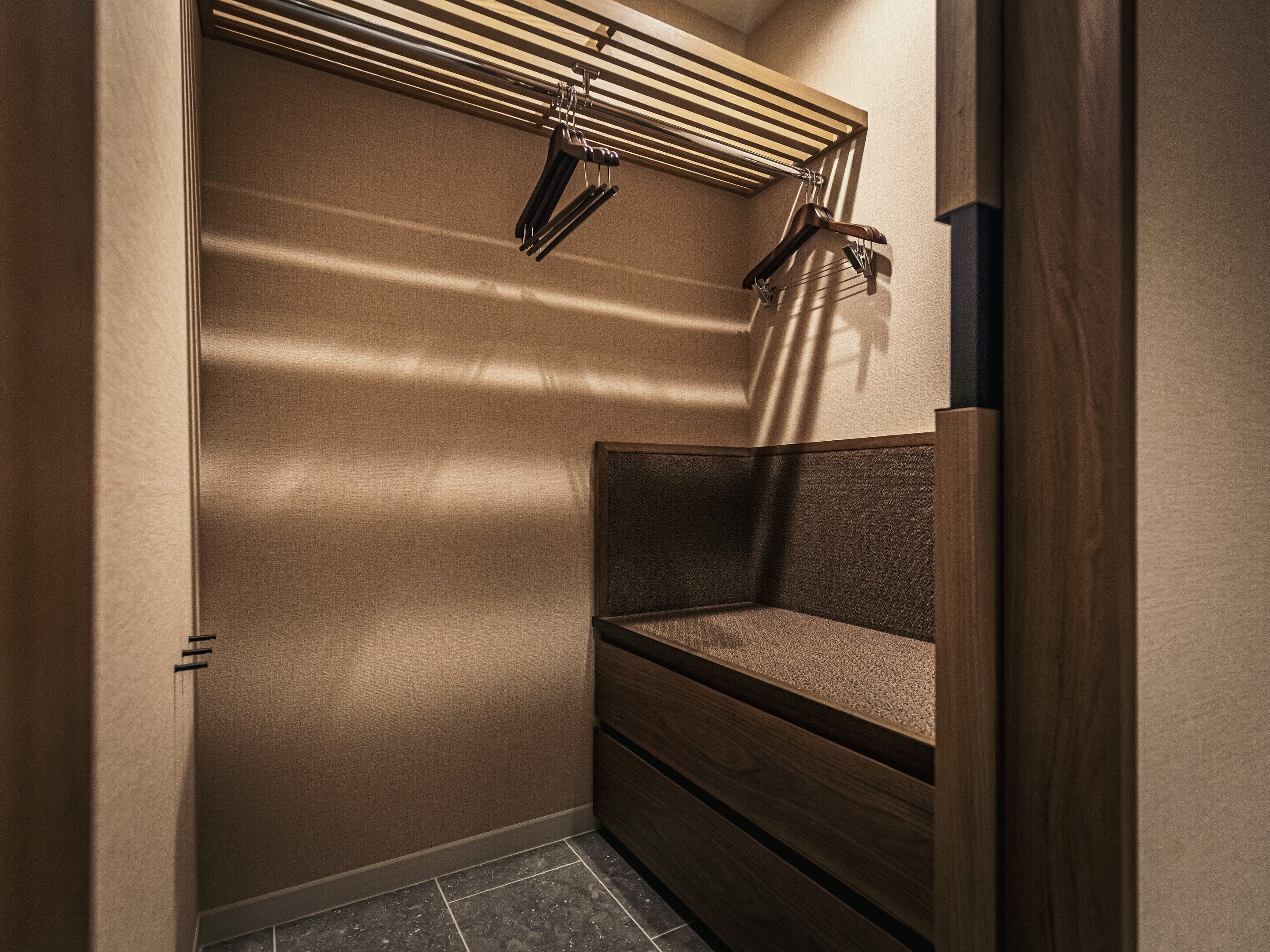 A corner of a room with a bench, a wall-mounted drying rack, and a textured wall.