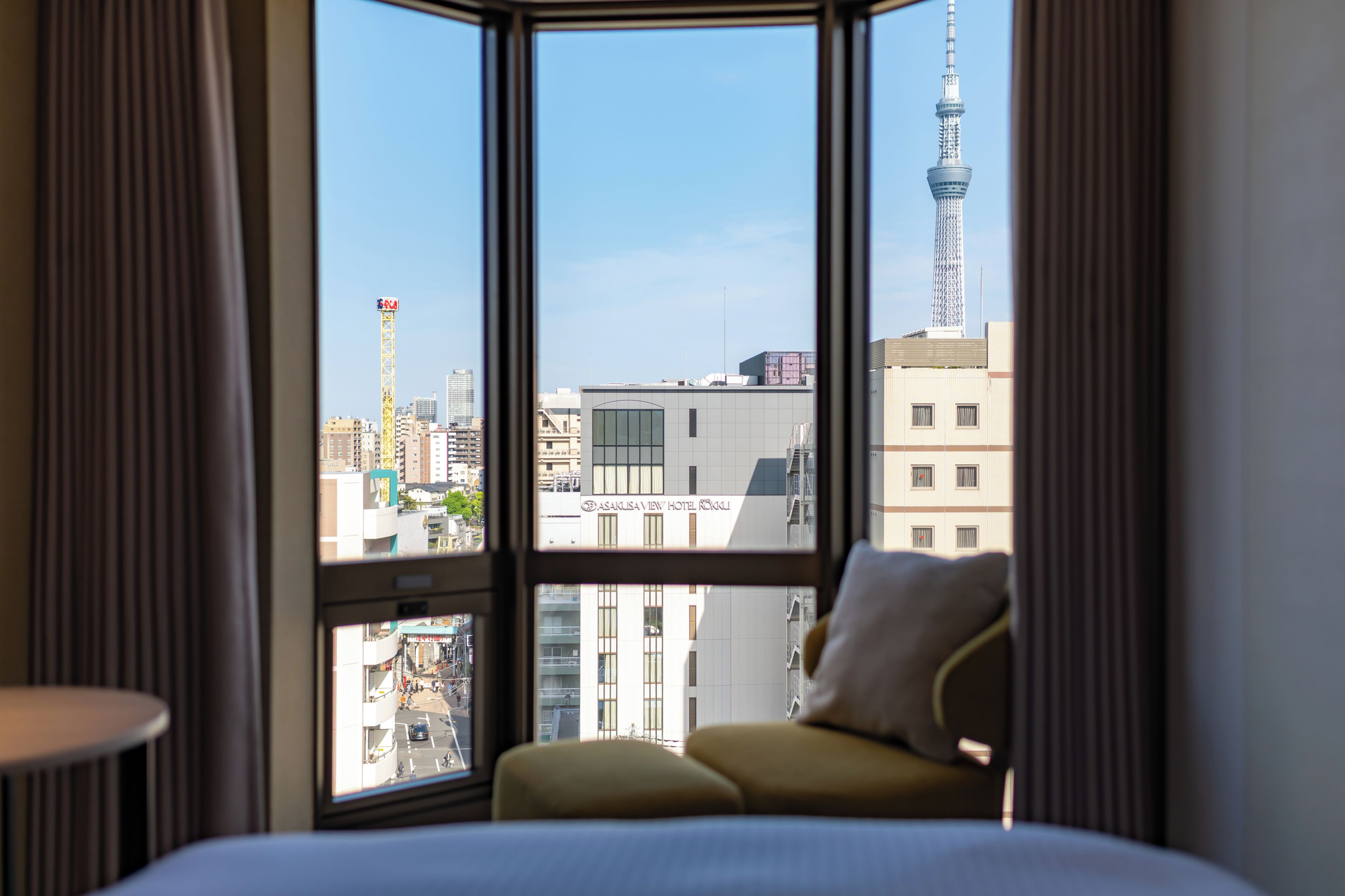 A hotel room with a large window offering a view of a cityscape, including a prominent tower.