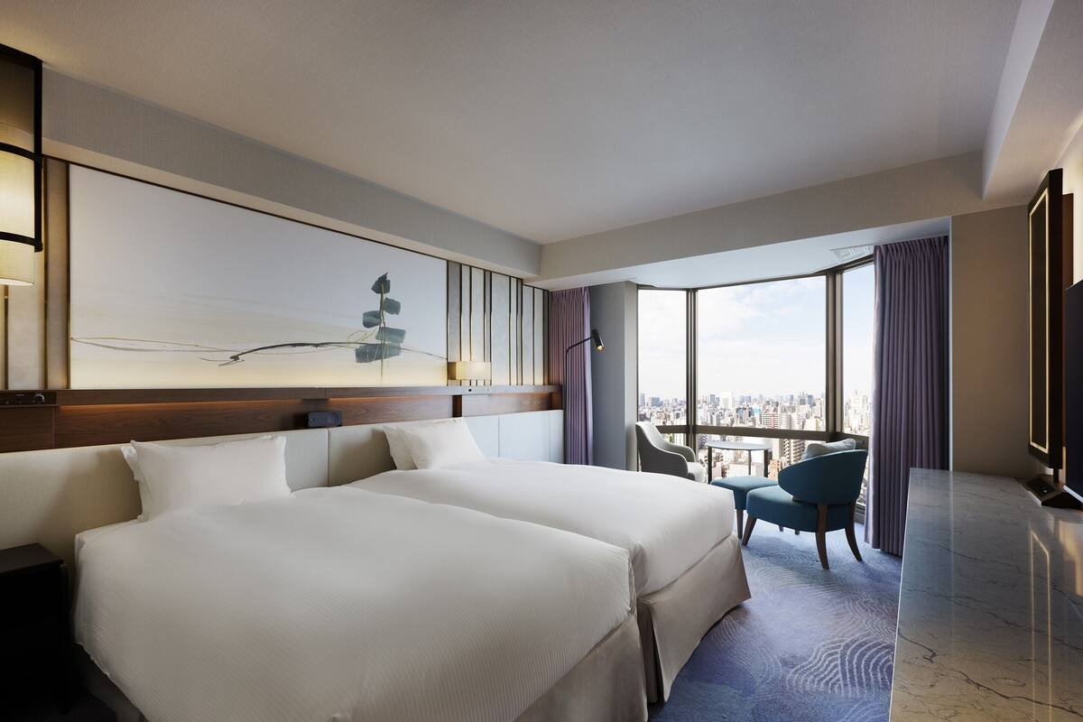 A hotel room with a large bed, a desk, a chair, and a view of the city.