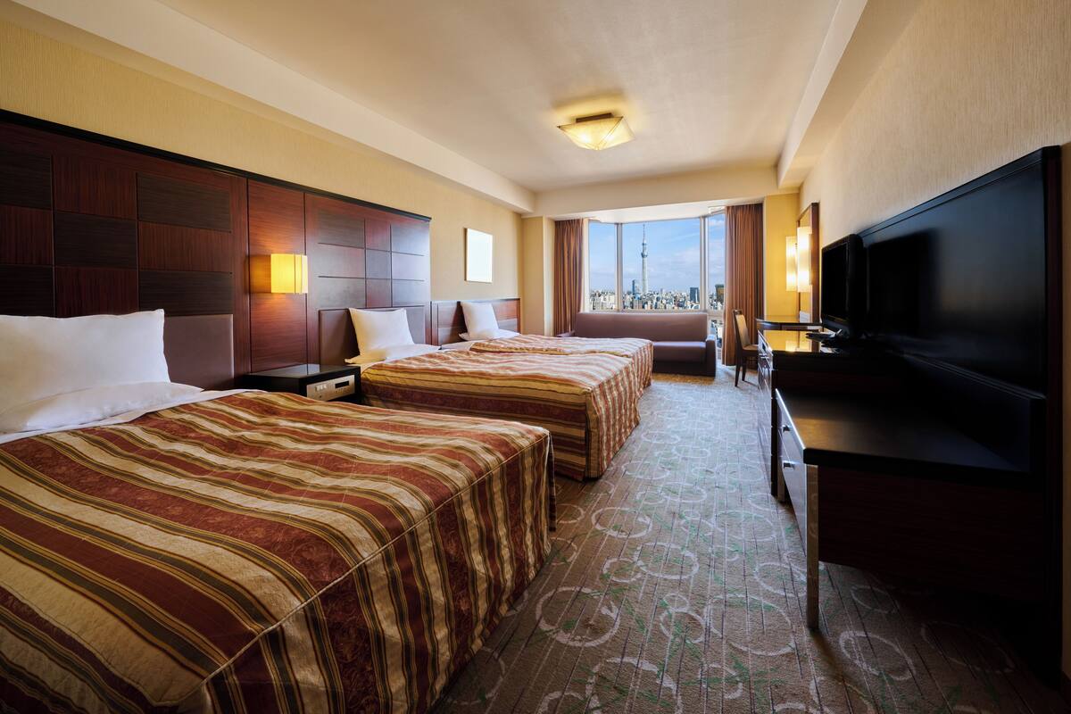 A hotel room with two beds, a TV, and a city view.