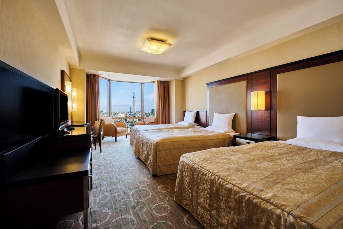 A hotel room with two beds, a TV, a desk, and a view of a cityscape.