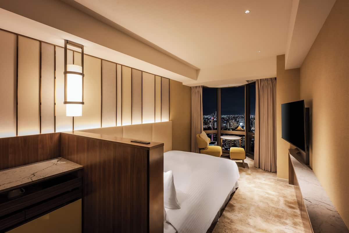 A hotel room with a bed, a desk, a TV, and a city view.