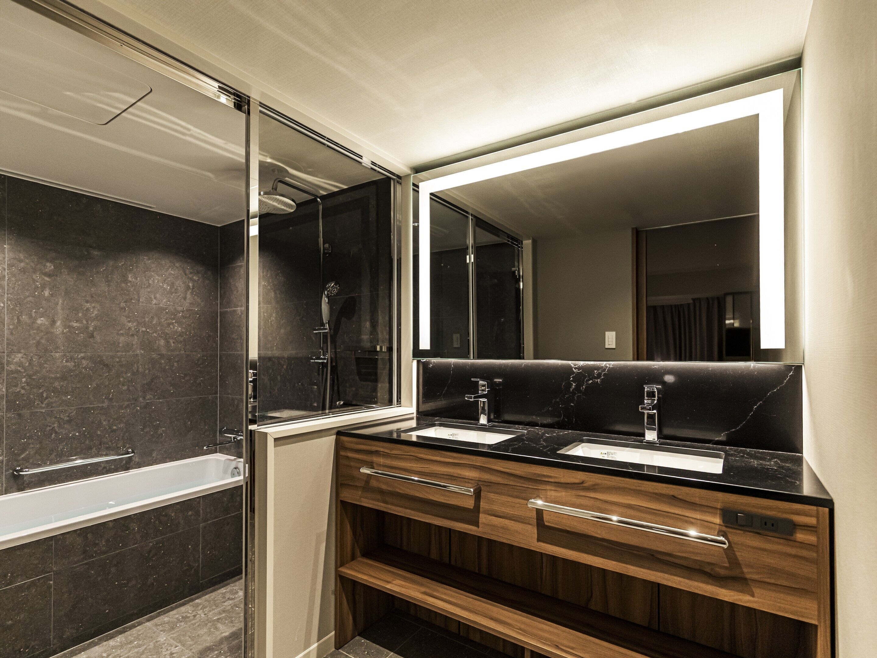 Un baño moderno con un espejo grande, dos lavamanos, una ducha y muebles de madera.