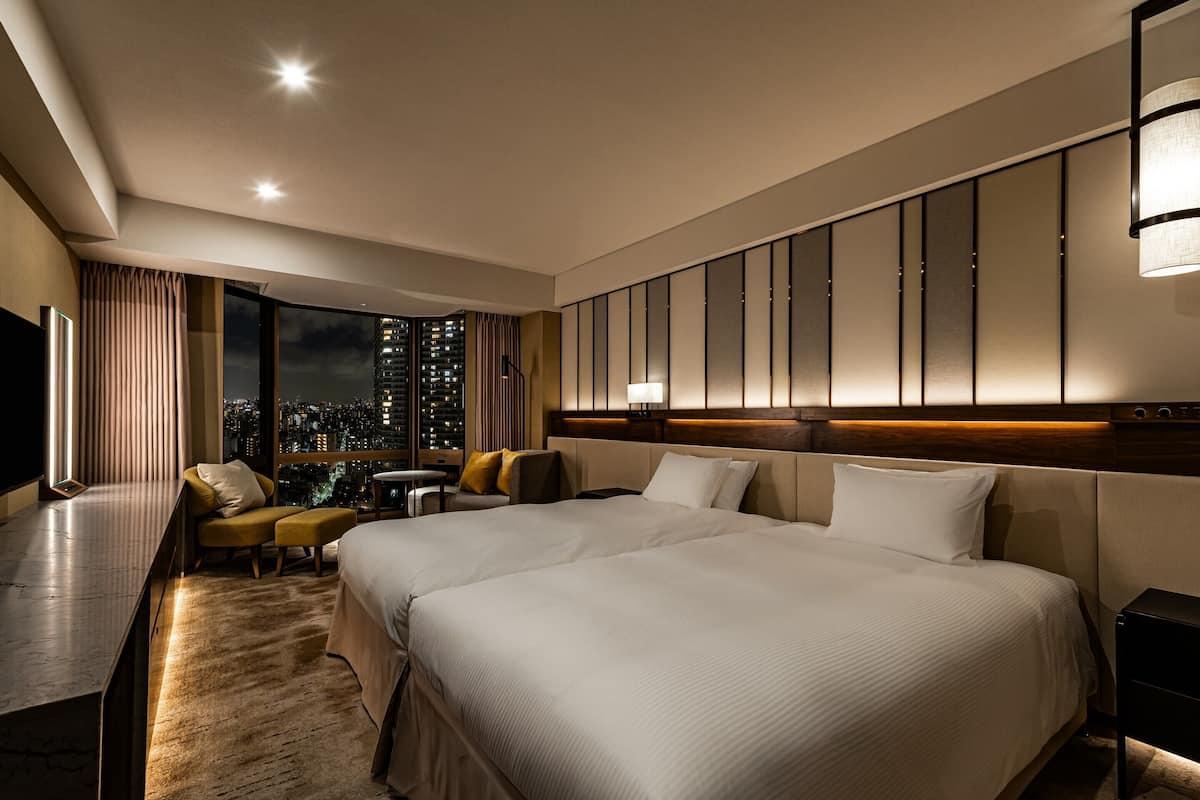 A hotel room with a large bed, a desk, a chair, and a view of the city at night.