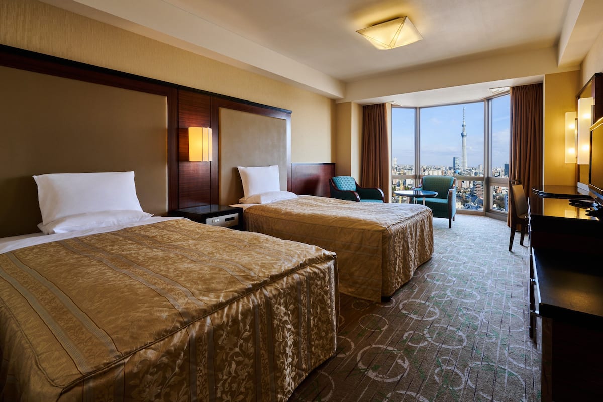 A hotel room with two beds, a desk, and a view of a cityscape.
