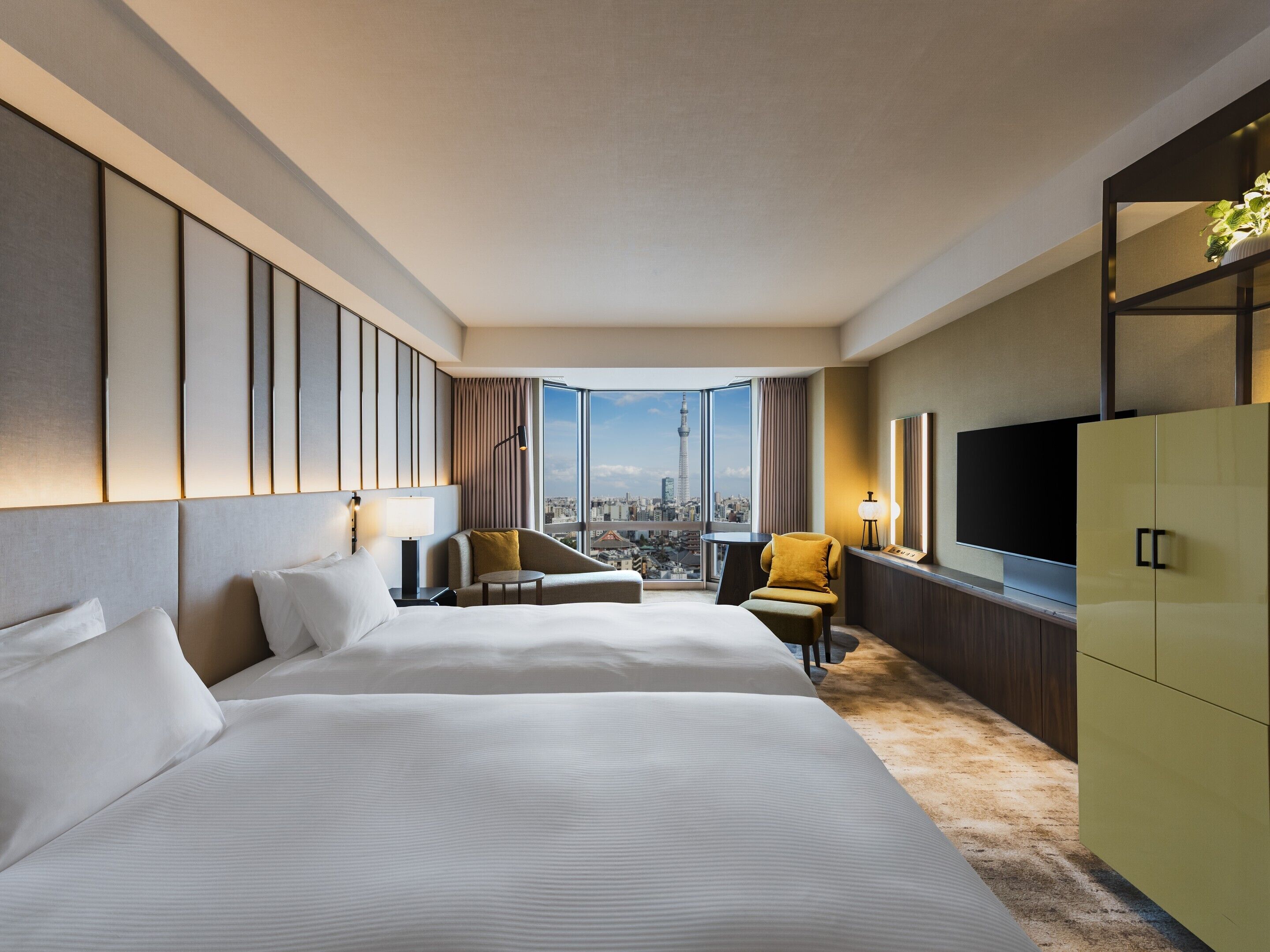 Habitación de hotel con dos camas, televisión, escritorio y vistas a la ciudad.