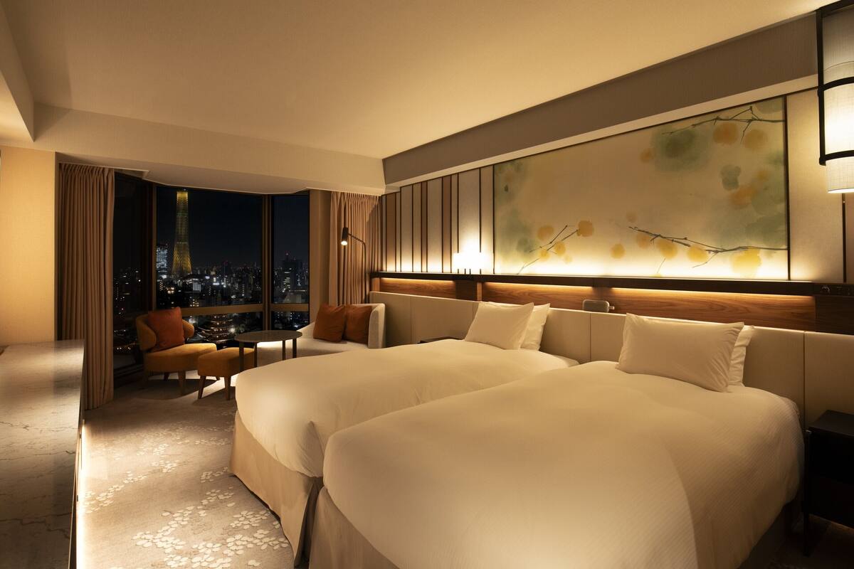 A modern hotel room with a large bed, a seating area, and a city view.
