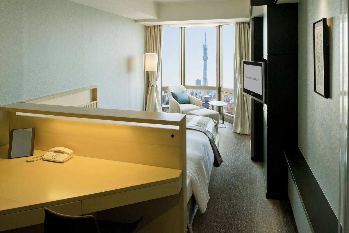 A hotel room with a desk, chair, bed, TV, and a city view.