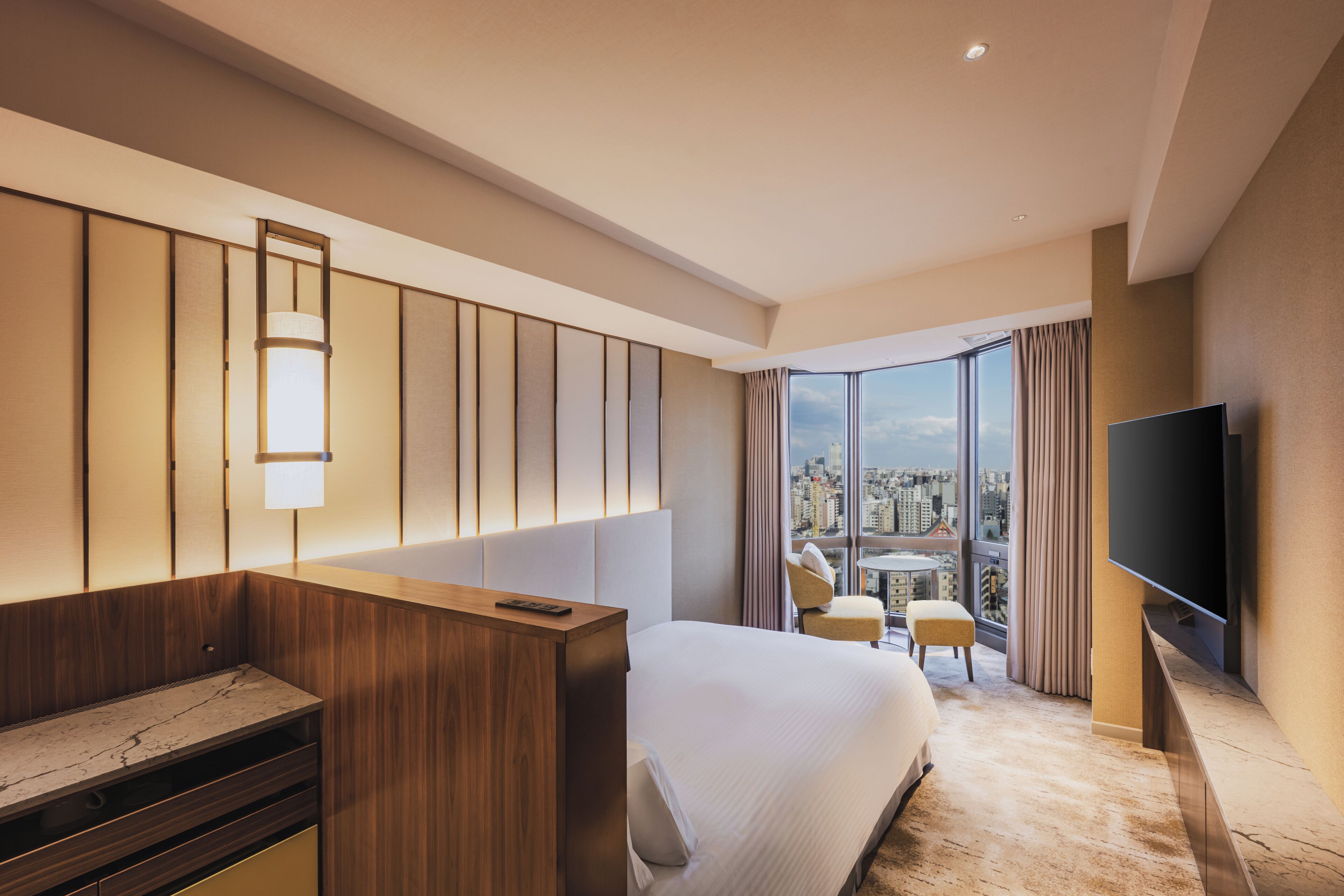 Une chambre d’hôtel moderne dotée d’un grand lit, d’une télévision, d’un bureau et offrant une vue sur la ville grâce à de grandes fenêtres.