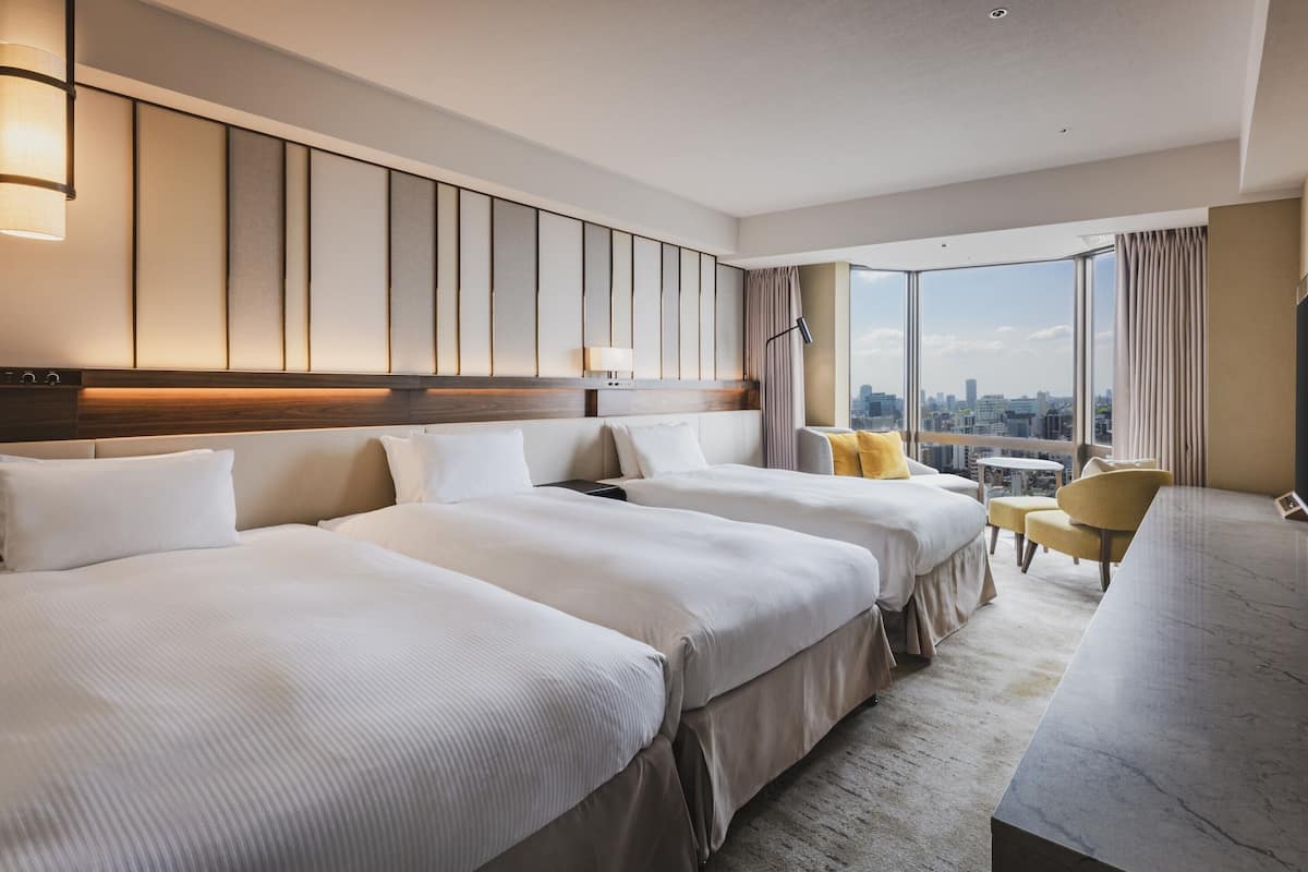 A hotel room with two beds, a desk, a chair, and a city view.