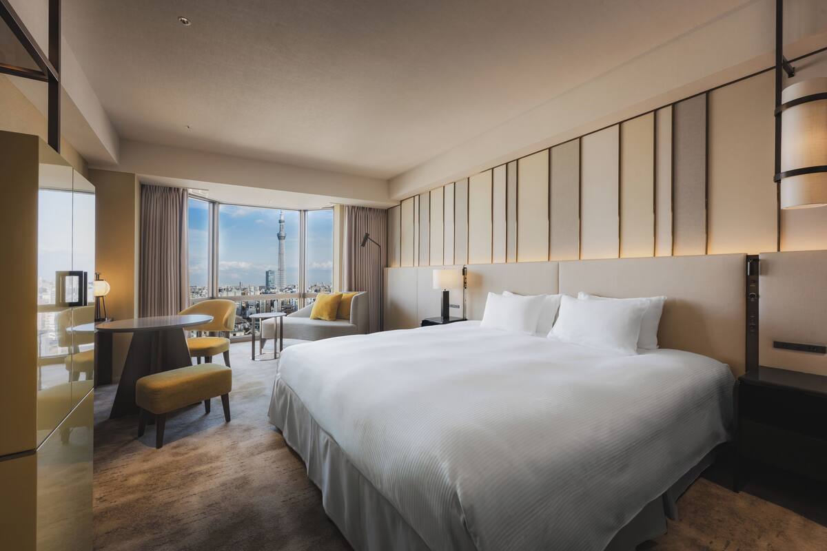 A modern hotel room with a large bed, a desk, and a view of a cityscape.