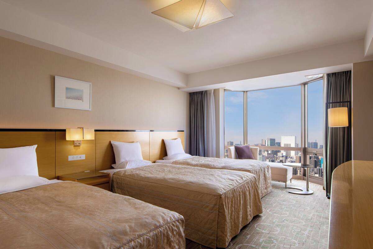 A hotel room with two beds, a city view, a large window, and a cityscape visible through the window.