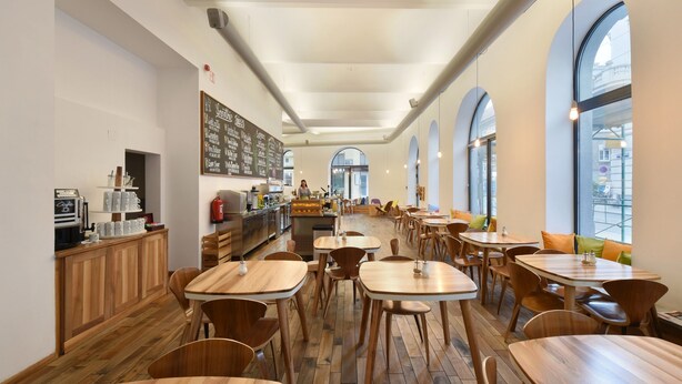 Un café spacieux avec des tables et des chaises en bois, un comptoir équipé pour préparer le café et de grandes fenêtres en arc de cercle.