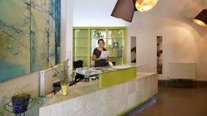 Un comptoir d’accueil avec une cloison en verre, une réceptionniste et un grand tableau abstrait accroché au mur.