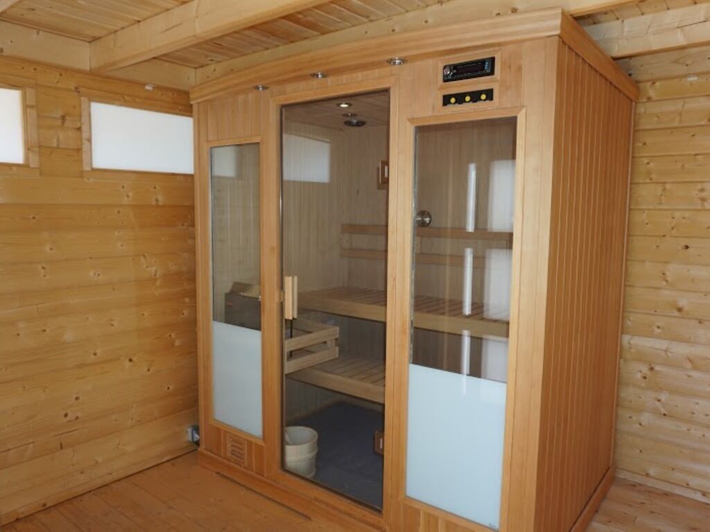 Eine Holzsauna mit Glastüren, einer Steuerung und einer Sitzbank im Inneren.