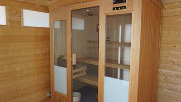 Eine Holzsauna mit Glastüren, einer Steuerung und einer Sitzbank im Inneren.