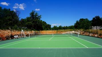 A tennis court with a net, benches, and trees in the background.