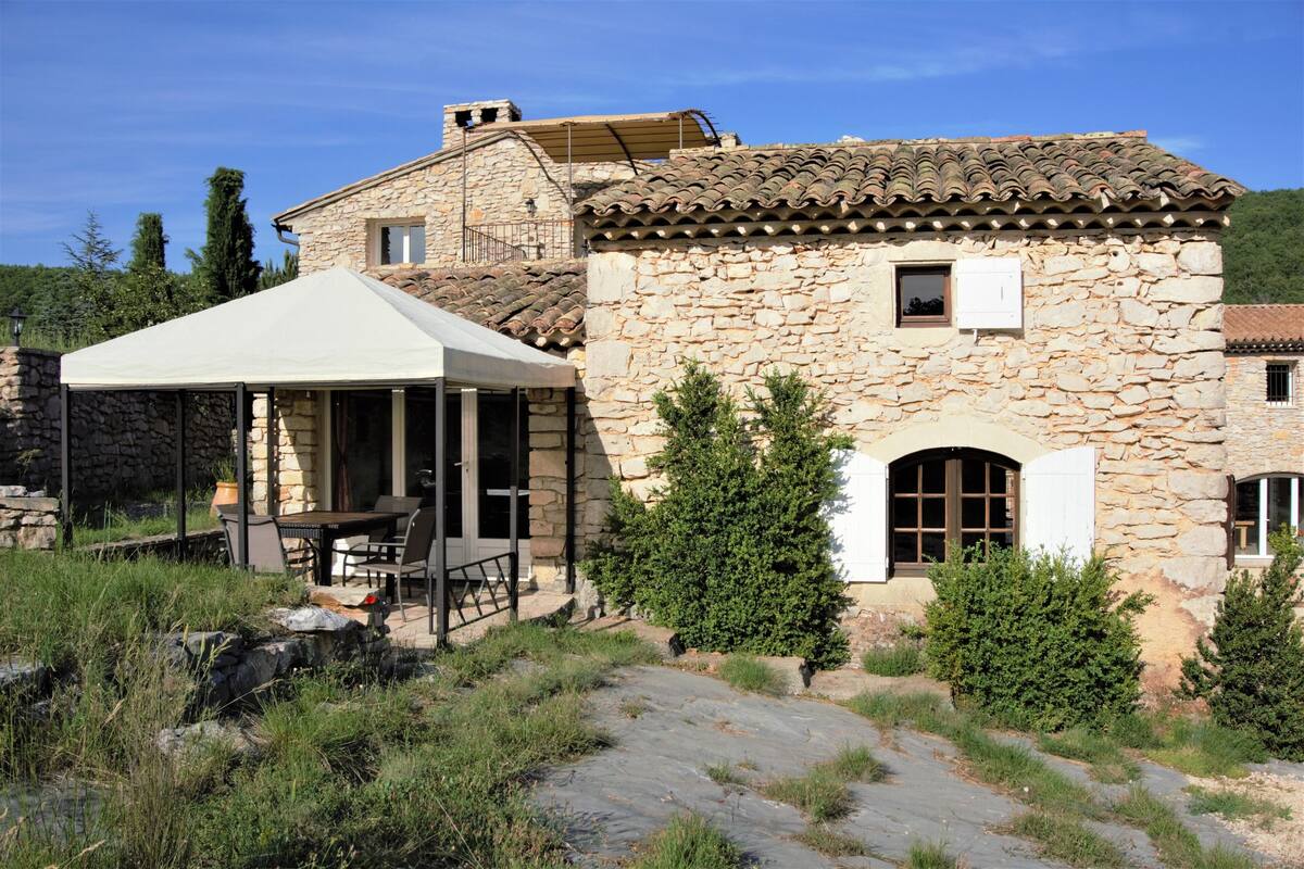A stone building with a tiled roof, a covered patio with outdoor furniture, and a stone pathway leading to the entrance.