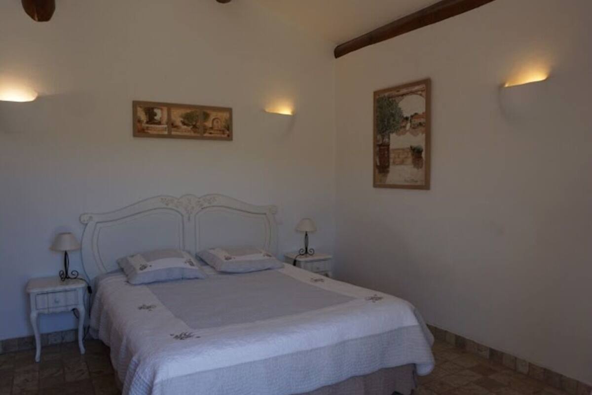 A bedroom with a large bed, two bedside tables with lamps, and two wall-mounted light fixtures.