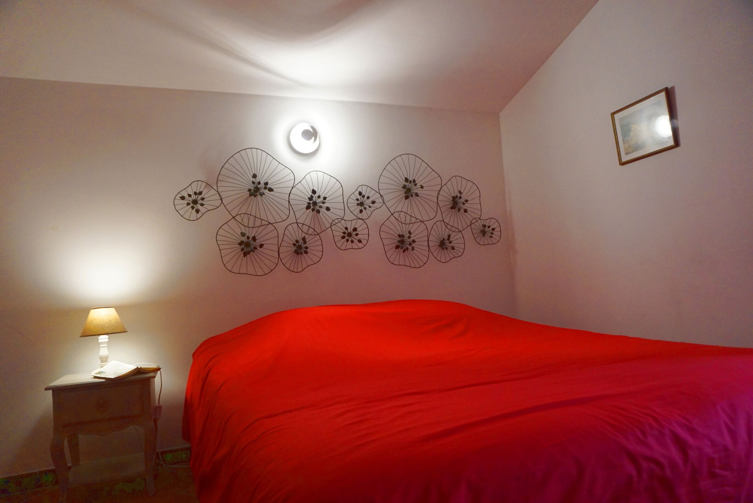 Una habitación con una cama, una lámpara de pared y una mesita de noche con lámpara.