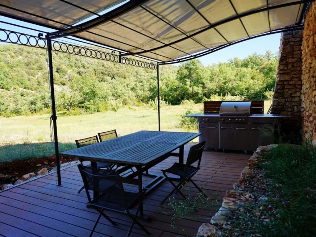 An outdoor patio with a table and chairs, a grill, and a stone wall.