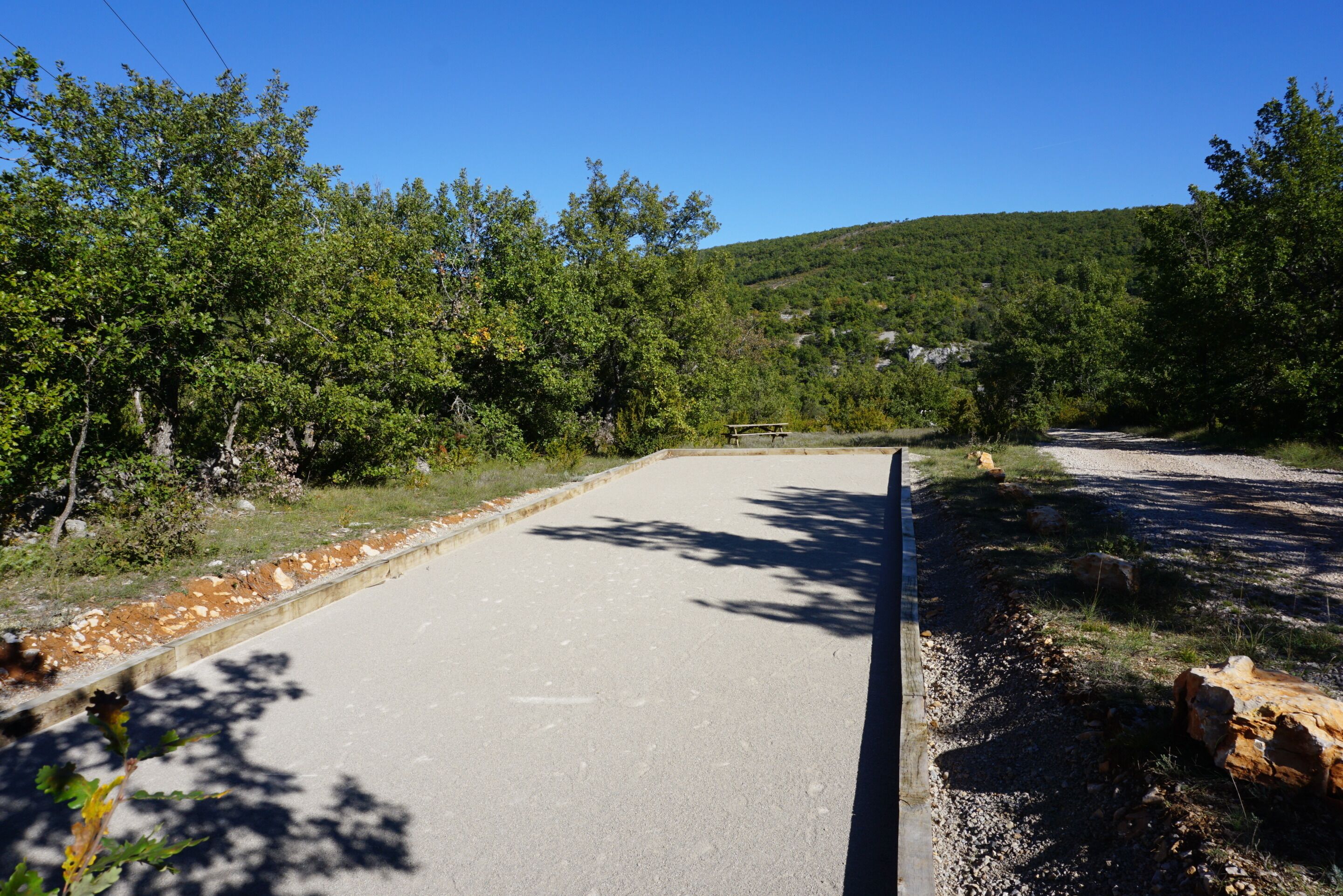 A paved area with a picnic table, surrounded by trees and a hilly landscape.
