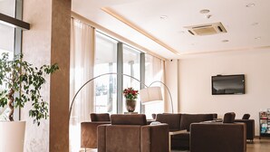 A modern living room with a sectional sofa, a floor lamp, and a potted plant. - Hotel Leone (Citluk)