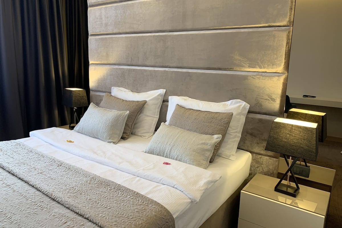 A modern hotel room with a large bed, two bedside tables, and a headboard with built-in lighting.