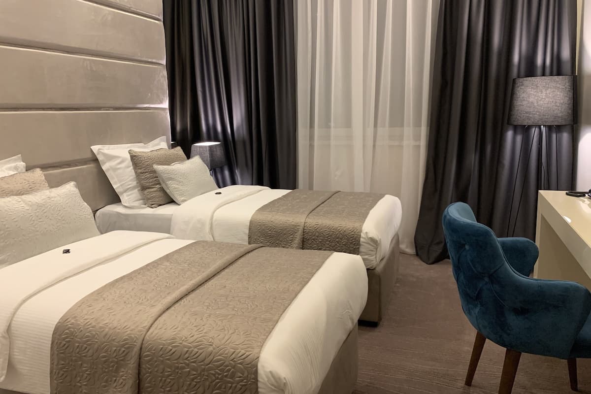 A hotel room with two beds, a desk, a chair, and a lamp.