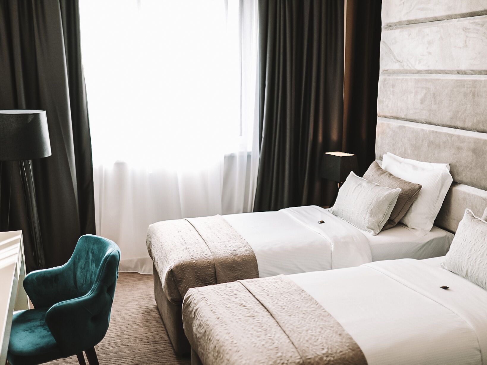 A hotel room with two beds, a desk, a chair, and a large window with curtains.