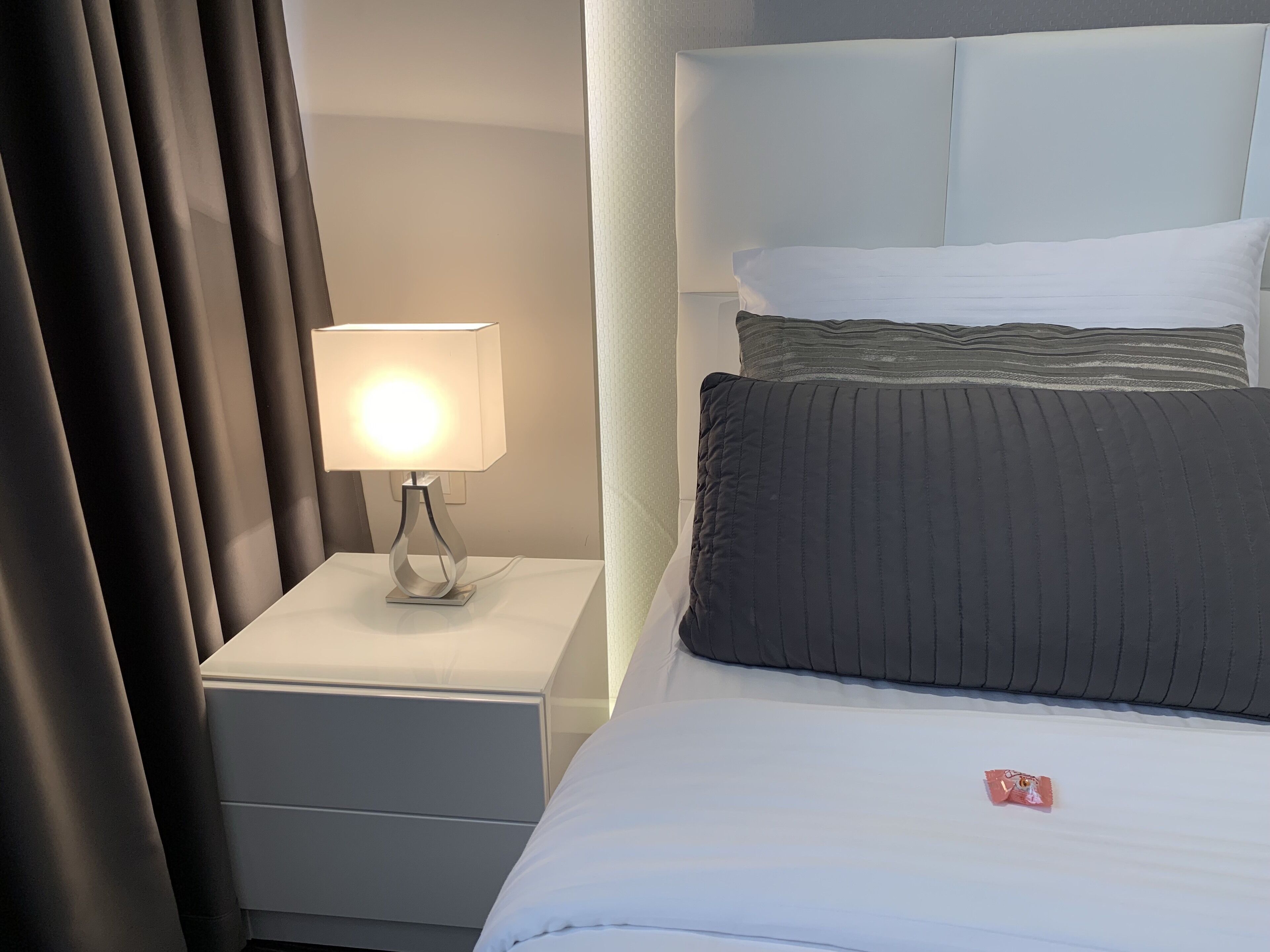 A neatly made bed with white and gray bedding, a bedside lamp, and a nightstand.
