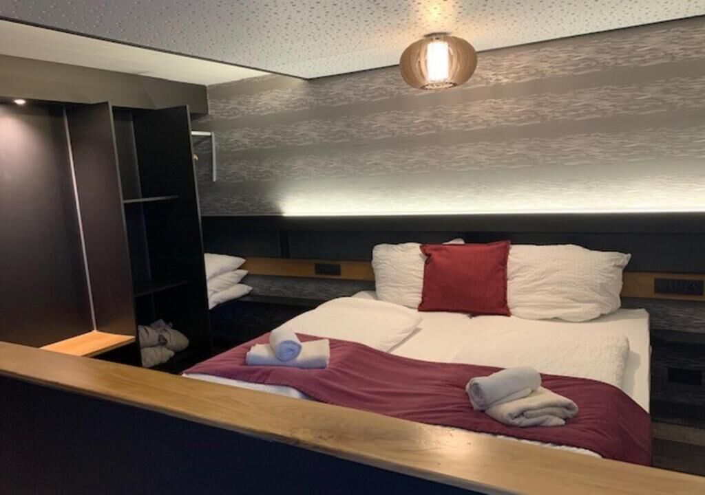 Une chambre d’hôtel moderne avec un grand lit, une tête de lit en bois, une armoire et un luminaire au plafond.