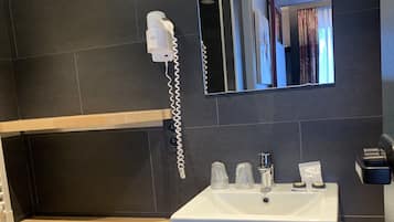 A modern bathroom with a white sink, dark tiles, a mirror, and a towel dispenser.