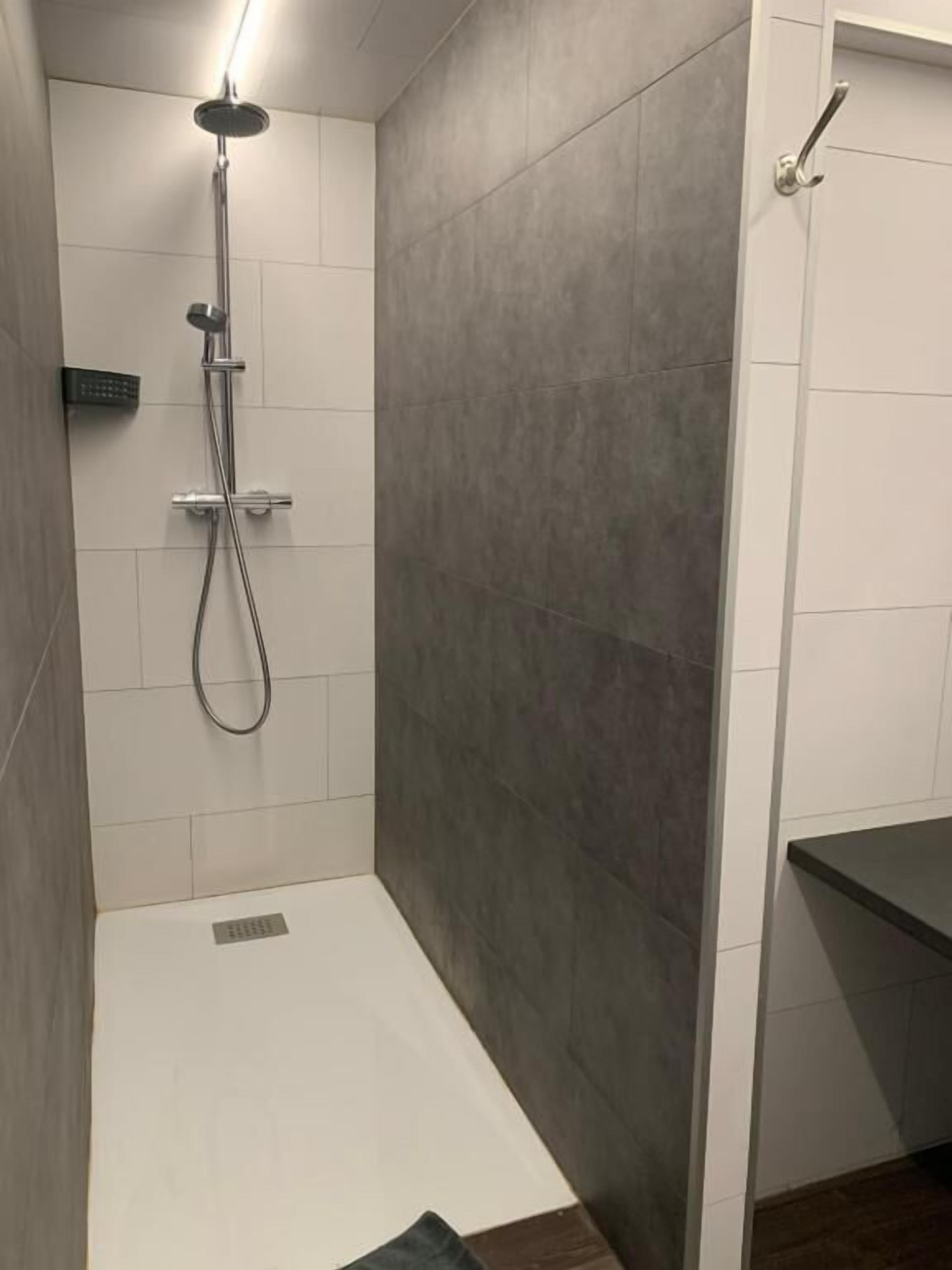 A modern bathroom with a shower, a control panel, and a dark-colored sink.