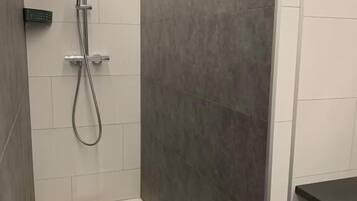 A modern bathroom with a shower, a control panel, and a dark-colored sink.