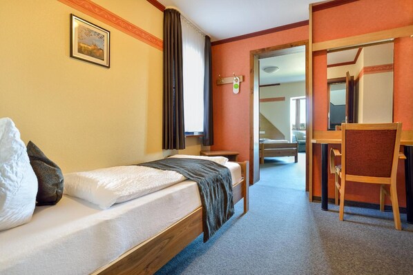 Habitación de hotel con una cama individual, un escritorio y una silla. Hay un cuadro en la pared y una ventana con cortinas.
