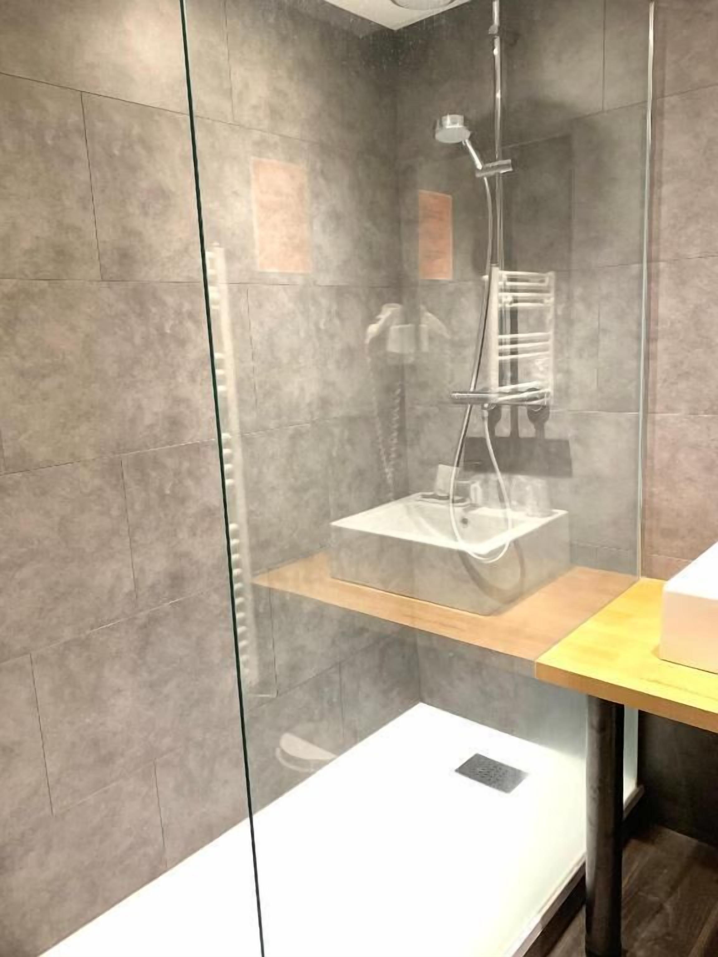 A modern bathroom with a glass-enclosed shower, a wooden shelf, and a white countertop.