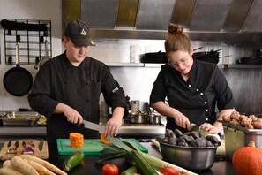 Two individuals in a kitchen preparing food with vegetables and potatoes visible. - Hôtel du Lac (Buetgenbach)