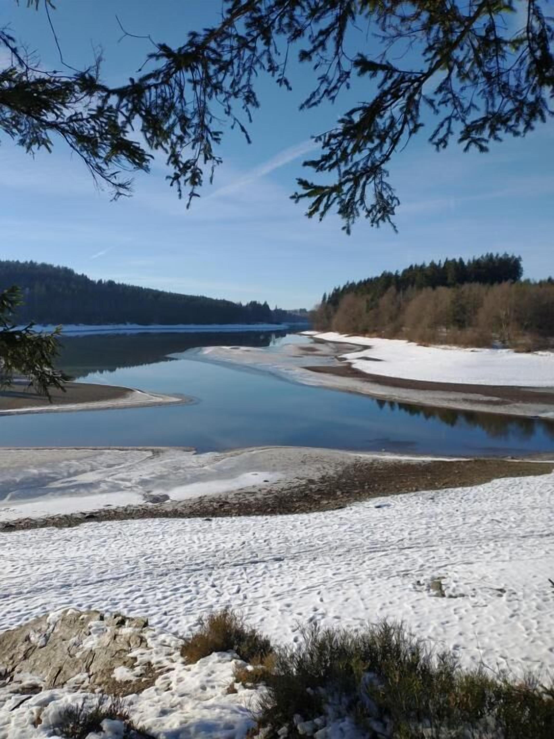A snowy landscape with a river, trees, and a clear sky.