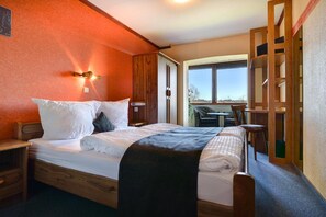 A bedroom with a large bed, wooden headboard, a nightstand, a desk with a chair, and a view of the outdoors through a large window. - Hôtel du Lac (Buetgenbach)