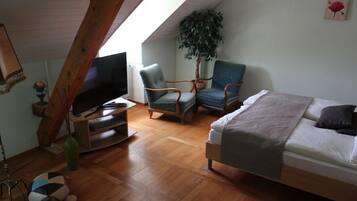 A cozy room with a bed, two armchairs, a television, and a large plant.