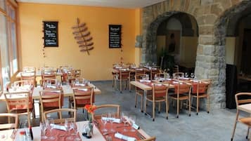 Un restaurant doté de nombreuses tables et chaises, d’arches en pierre et de tableaux noirs affichant les plats à la carte.