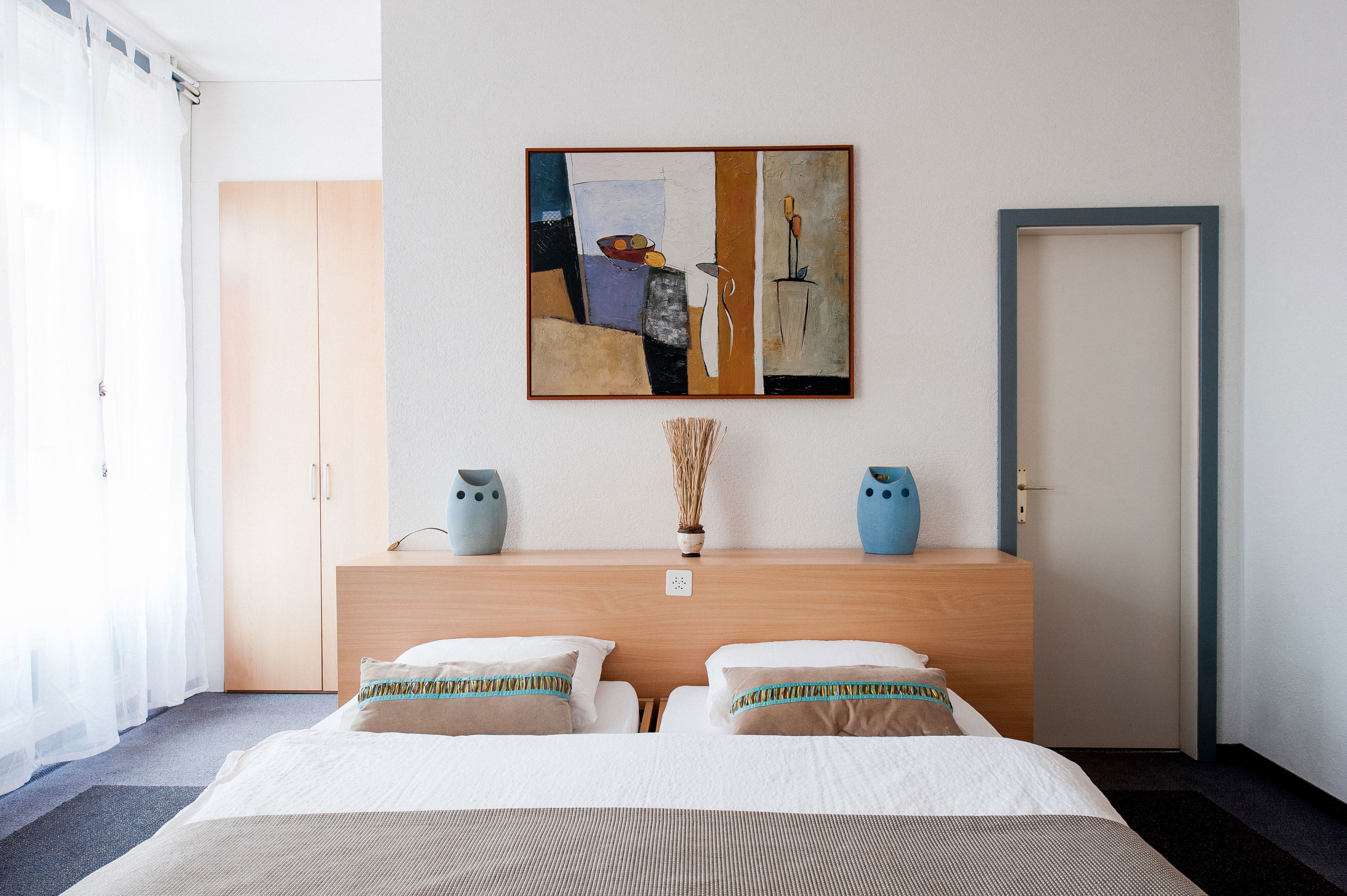 Een hotelkamer met een bed, een houten hoofdeinde, een schilderij en een vaas met gedroogde planten.