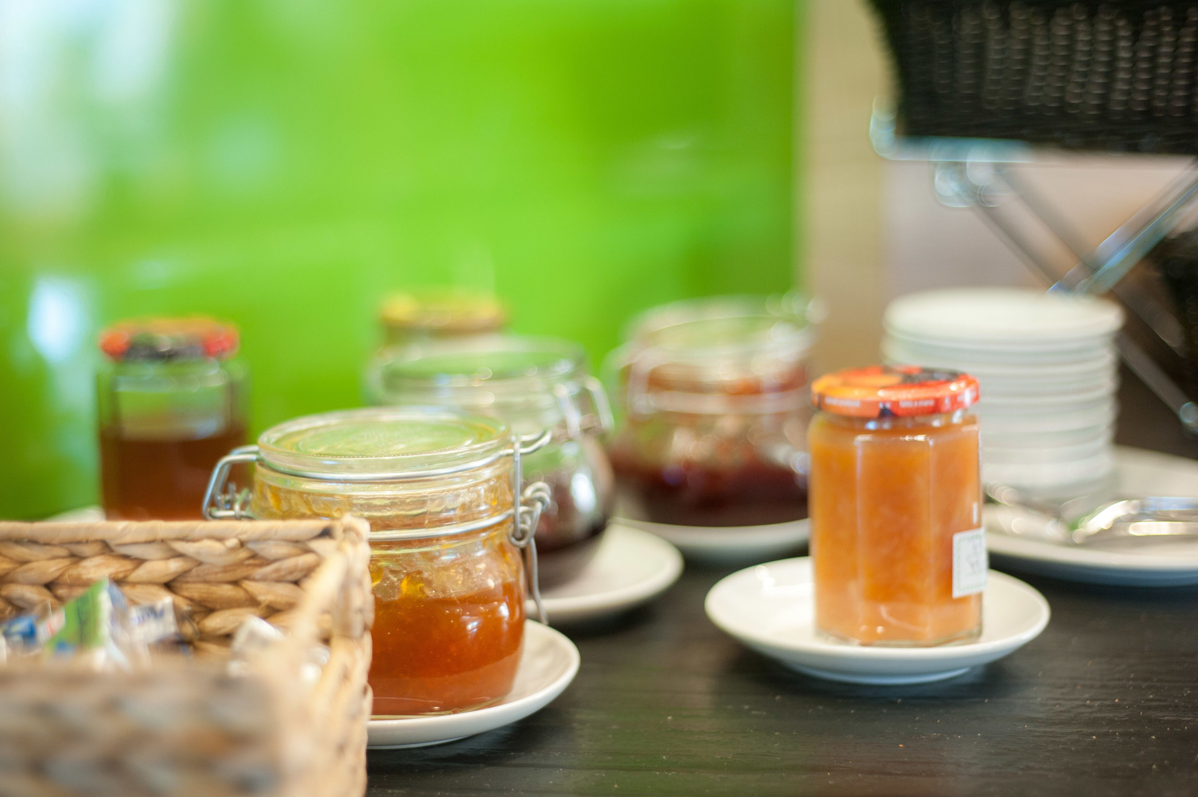 A table with various food items, including jars of preserves and a basket of bread.