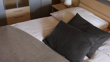 Una cama bien hecha con un edredón gris y blanco, un cabecero de madera y una mesita de noche con una lámpara.