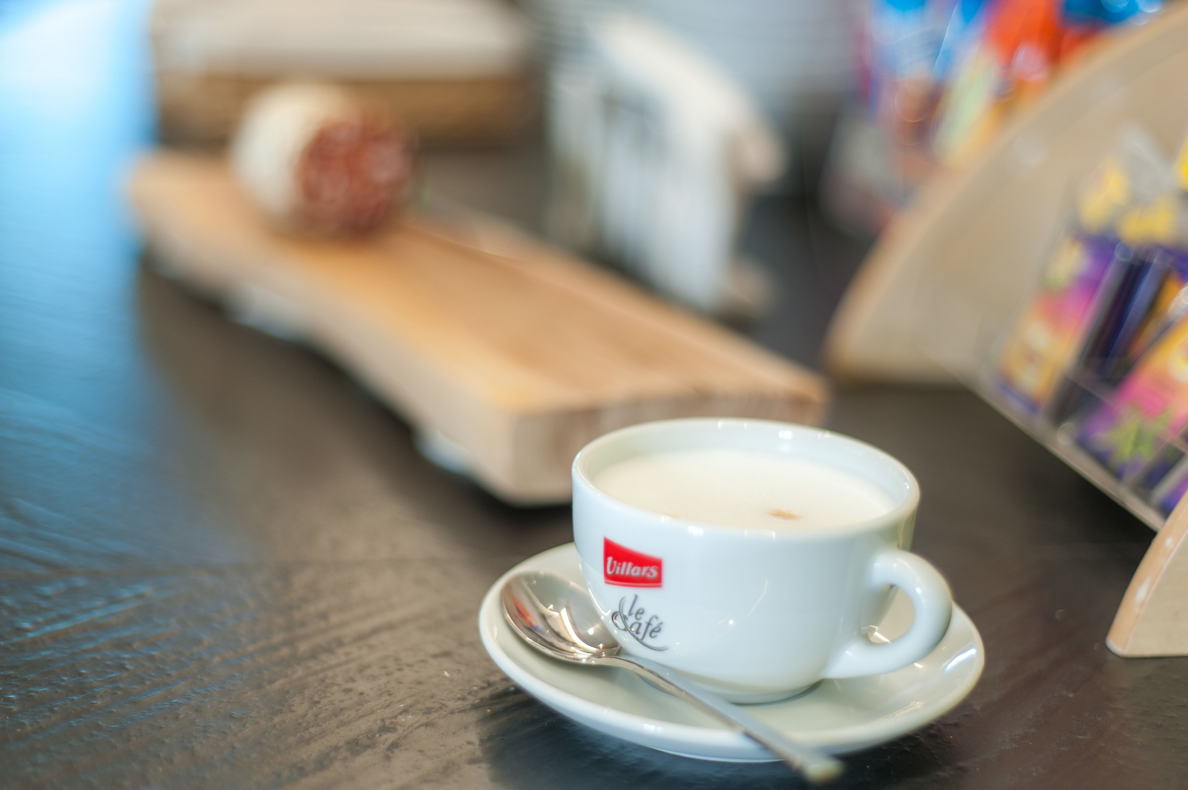 Una taza blanca con una cuchara sobre un plato, con la etiqueta 'Villers Café'.